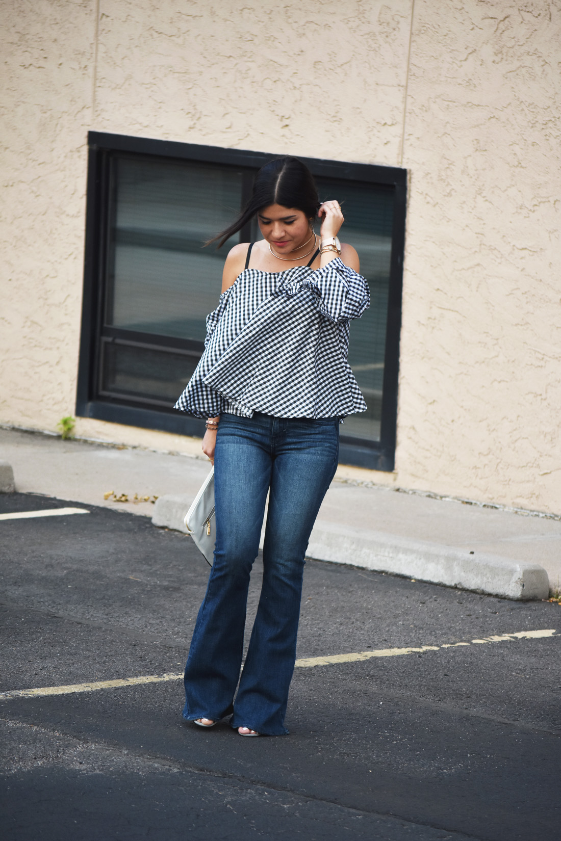 Carolina Hellal of Chic Talk wearing a chicwish gingham off the shoulder top, American Eagle bell bottom jeans, and le motto black and white clutch 