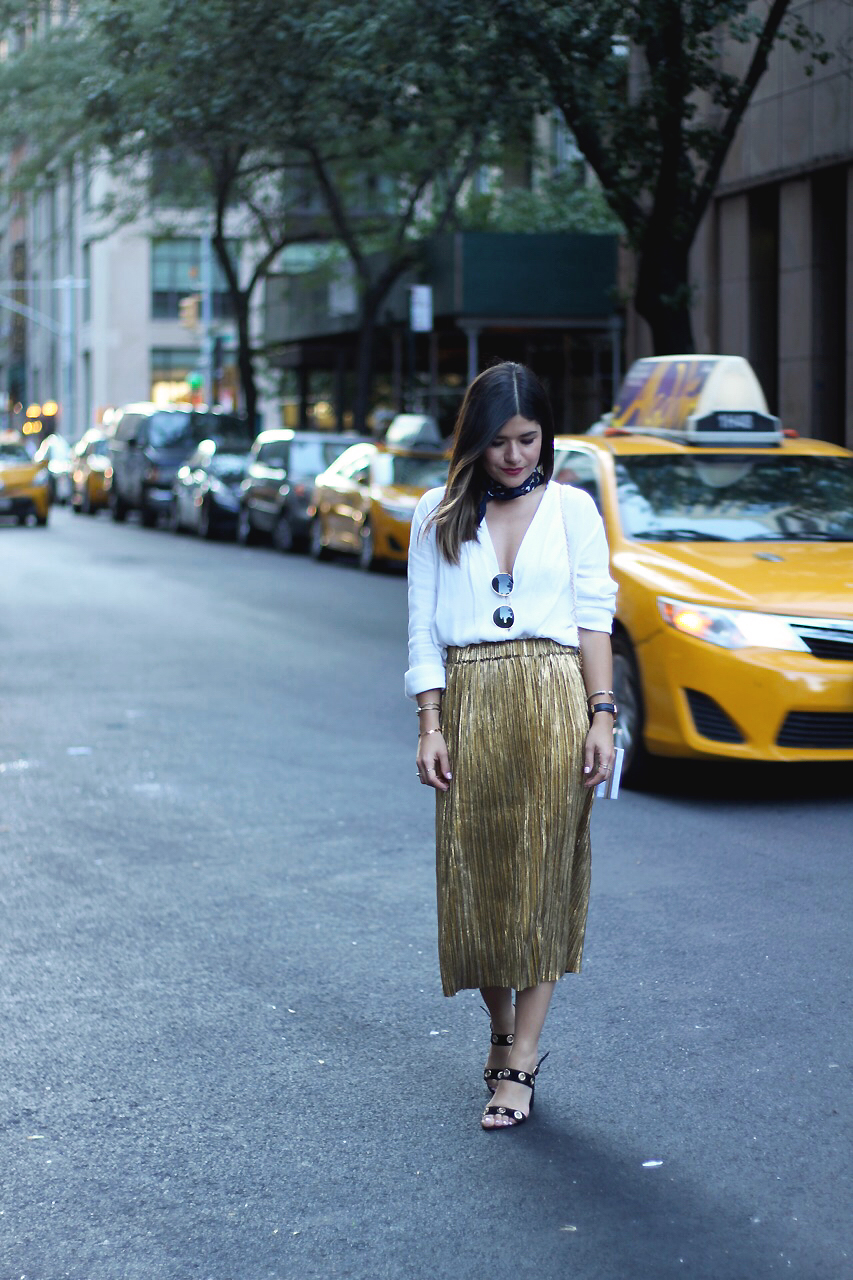 Carolina Hellal of Chic Talk during NYFW wearing a SheIn gold pelated skirt, white oversized draped top, and Public Desire black sandals