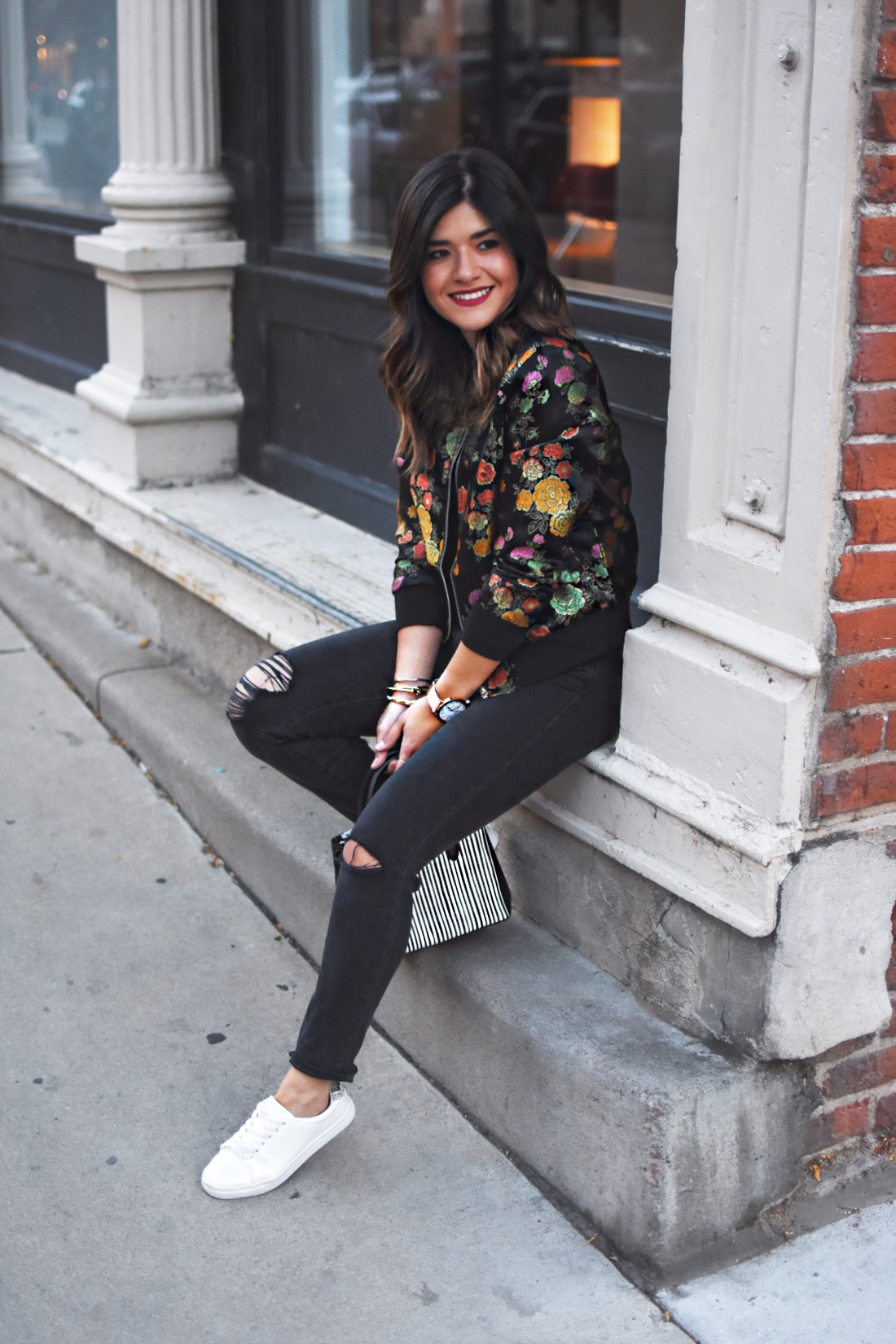 Carolina Hellal of Chic Talk wearing a VIPme floral bomber jacket, Madewell dark gray ripped jeans, h&m white sneakers, and Ralph Lauren striped bag