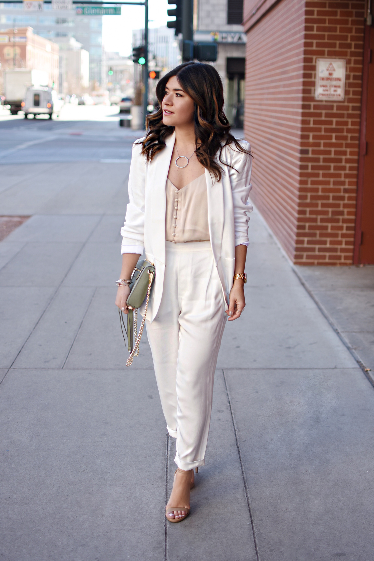 Carolina Hellal of CHIC TALK wearing a white suit via THACKER NYC, a Rebecca Minkoff bag, Steve Madden sandals, and NA-KD nude camisol