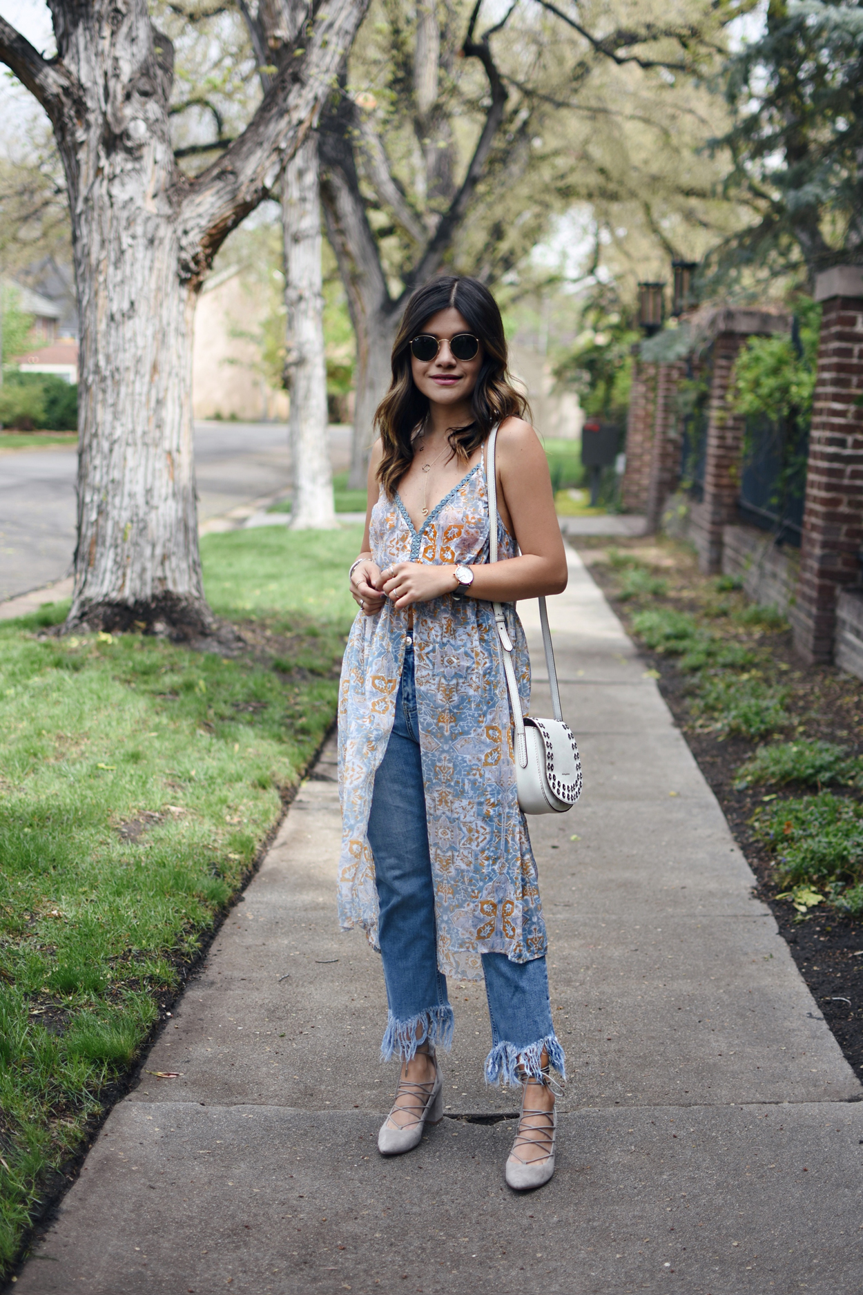 Carolina Hellal of Chic Talk wearing a floral tunic, fringed jeans, lace up heels, Rounded Rayban sunglasses and a white crossbody bag