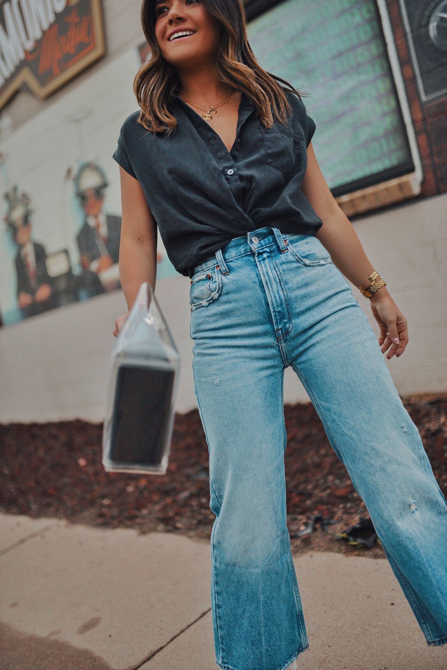 Carolina Hellal of Chic Talk wearing Abercrombie & Fitch wide leg jeans and a black crop shirt, Steve Madden black strap sandals and clear STAUD clothing bag
