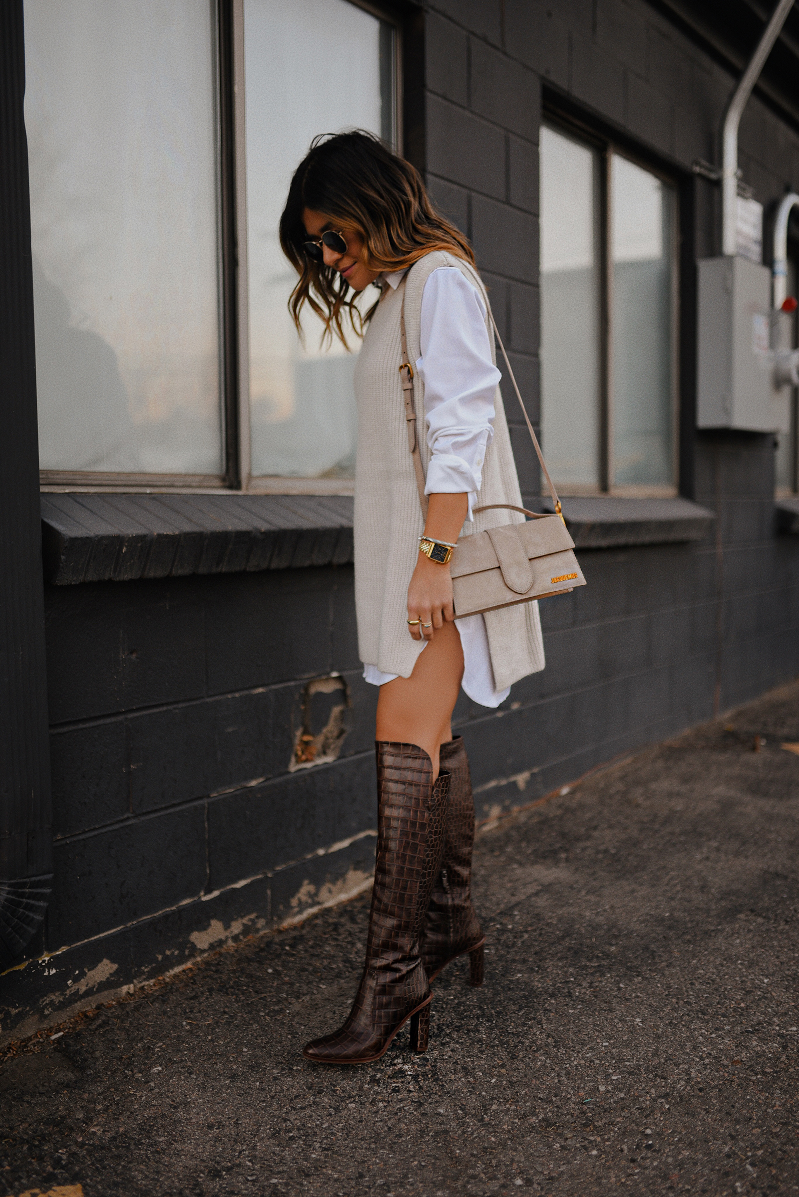Carolina Hellal of Chic Talk wearing an H&M sleeveless knit sweater, LEZE white button down, Jacquemus Le Bambino bag and Vince Camuto tall croc embossed boots. 