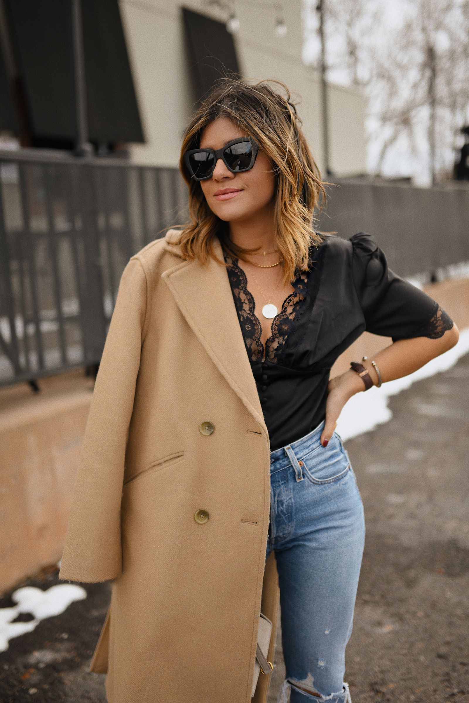 Carolina Hellal of Chic Talk wearing a WAYF black top with lace trims, Levi's 501 skinny jeans, Vince Camuto suede booties and Everlane camel coat. 