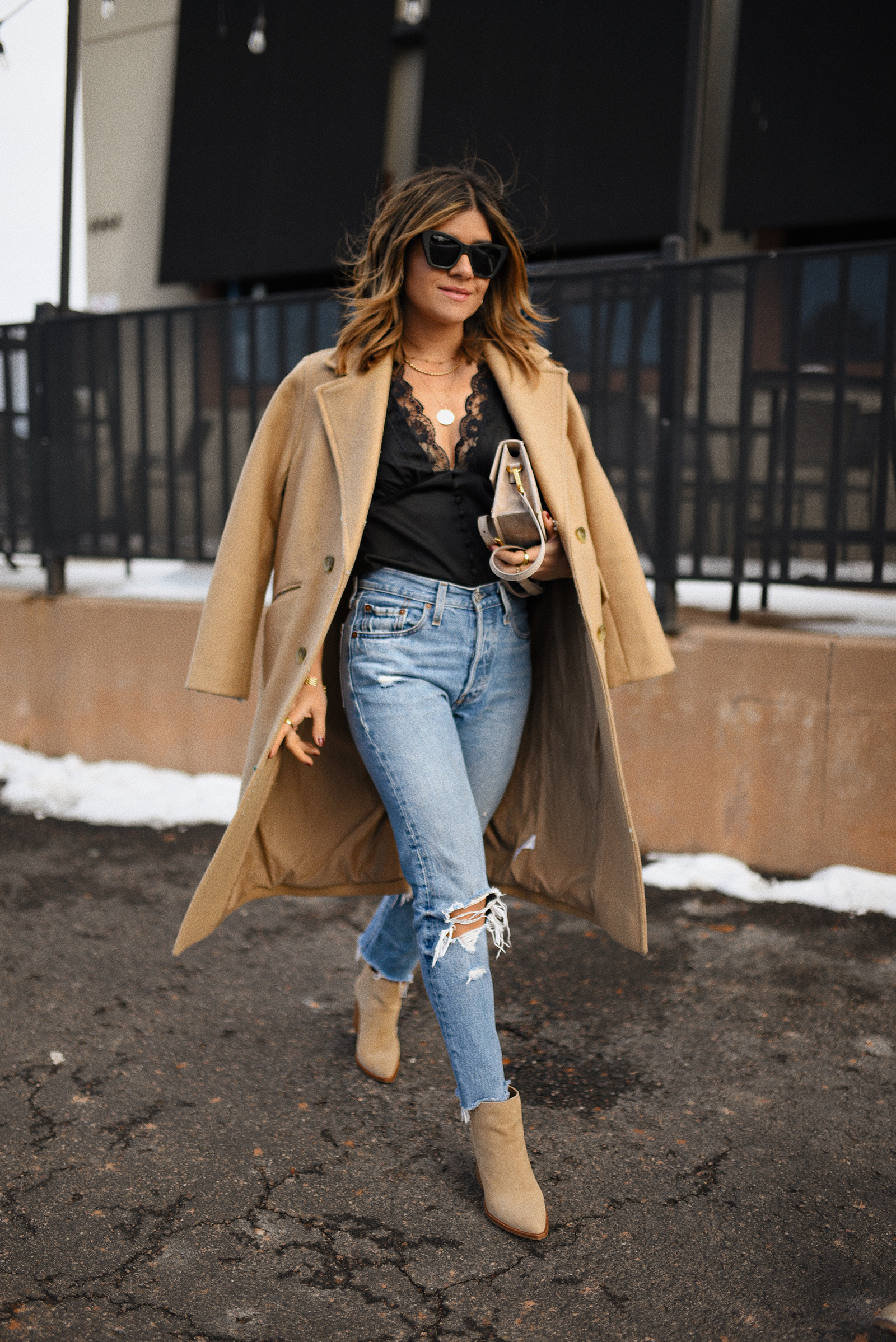 Carolina Hellal of Chic Talk wearing a WAYF black top with lace trims, Levi's 501 skinny jeans, Vince Camuto suede booties and Everlane camel coat. 