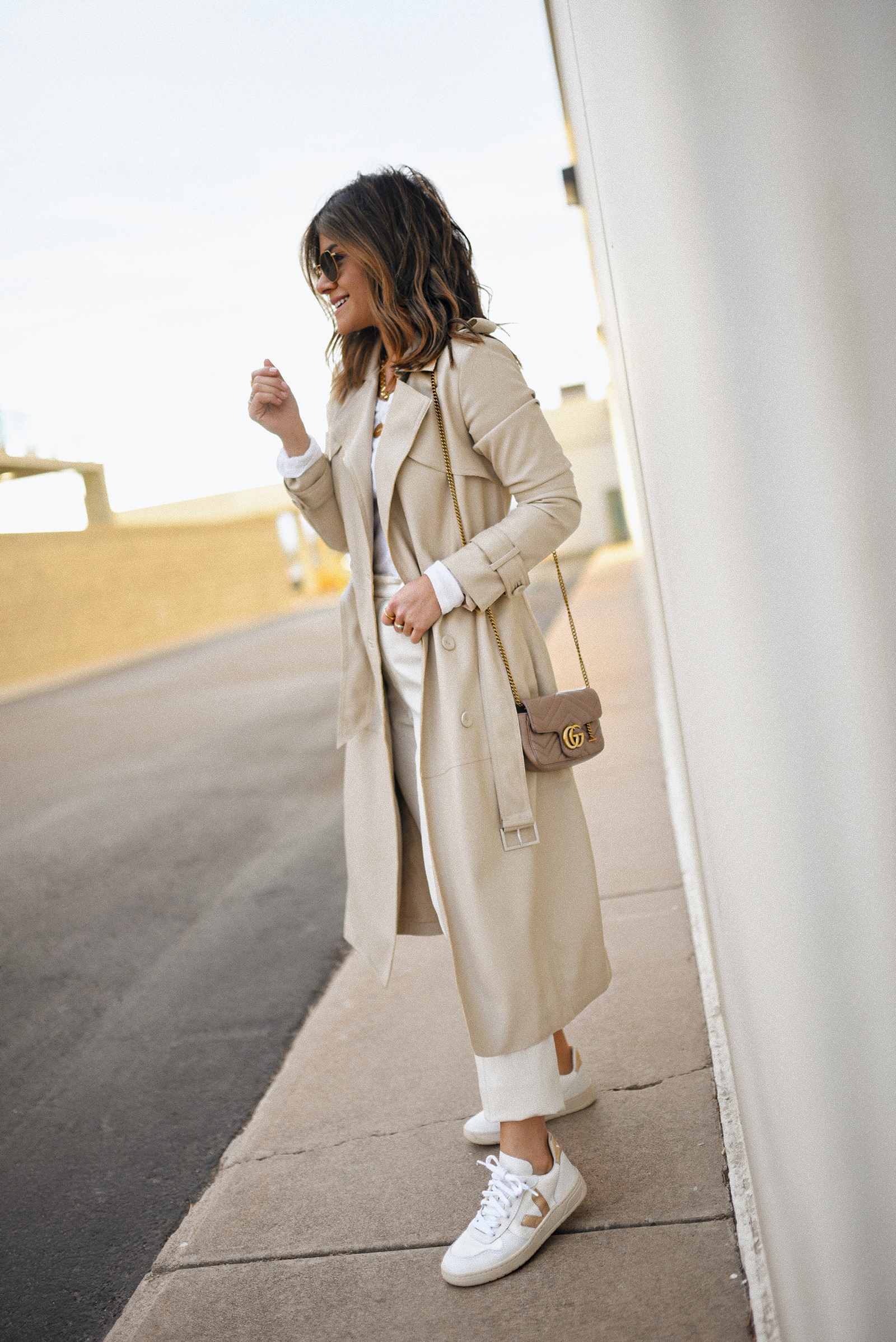 Carolina Hellal of Chic Talk wearing a Karen Millen faux leather trench coat, Michael Stars long sleeve white top, Uniqlo beige trousers and Veja sneakers. 
