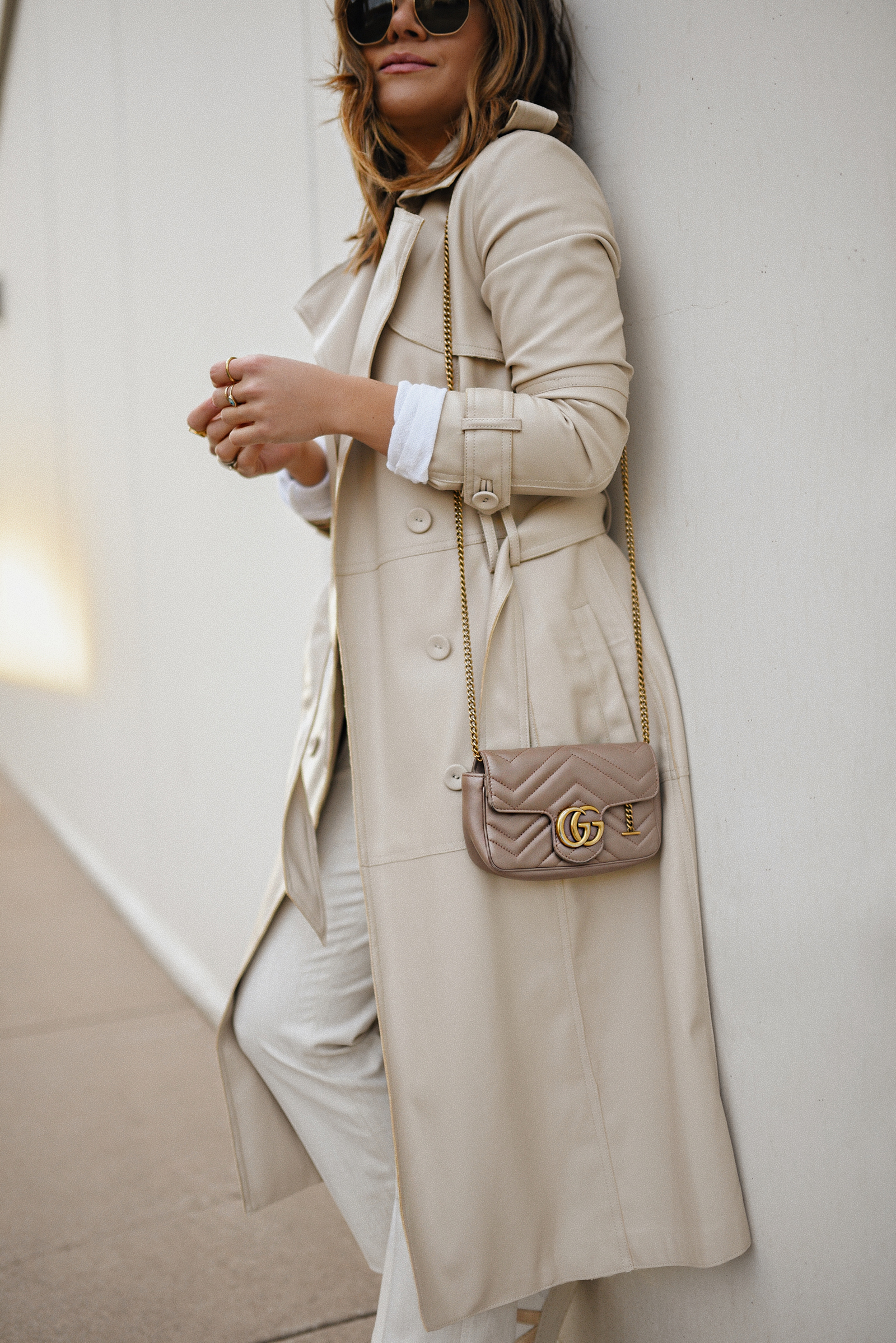 Carolina Hellal of Chic Talk wearing a Karen Millen faux leather trench coat, Michael Stars long sleeve white top, Uniqlo beige trousers and Veja sneakers. 