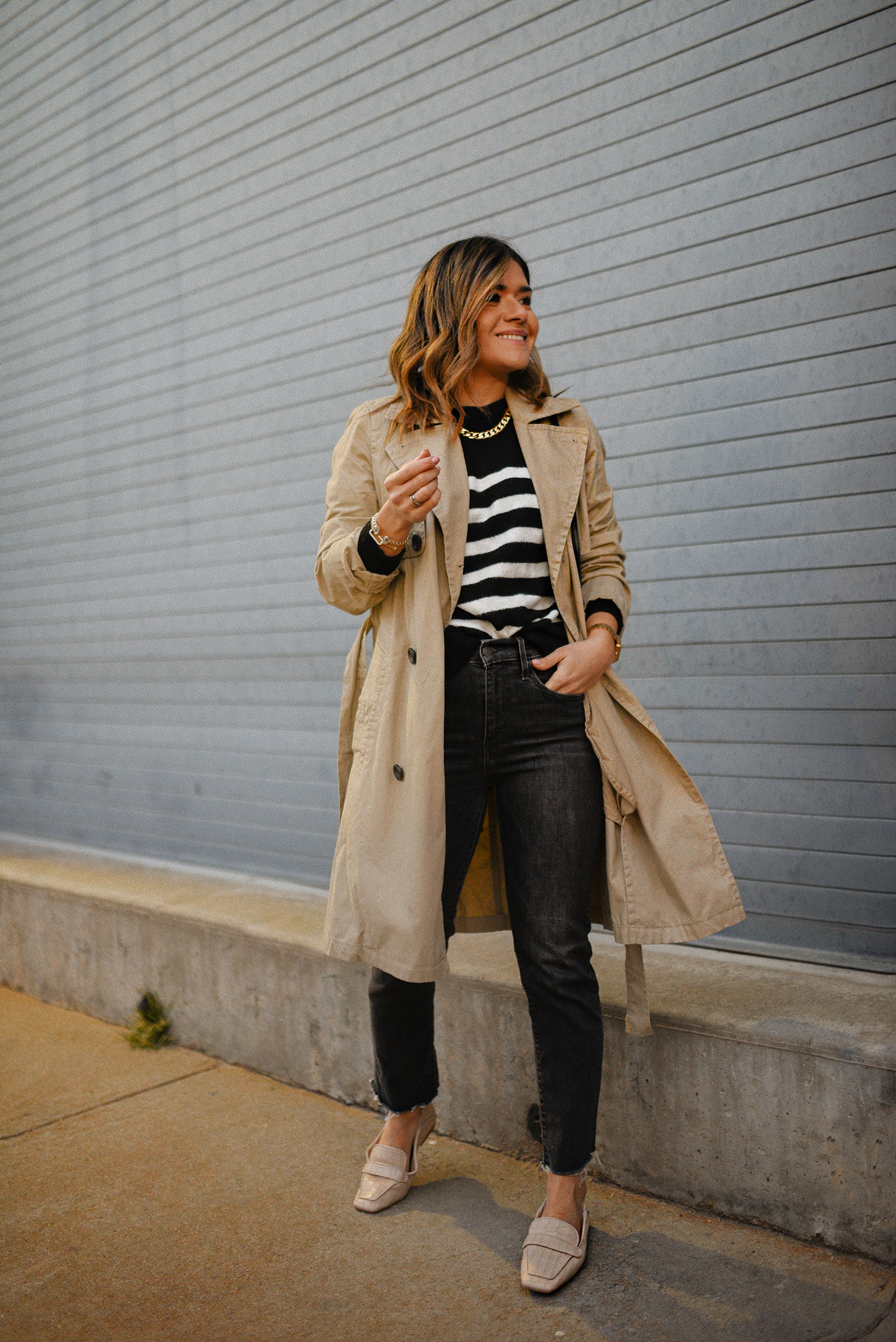 Carolina Hellal of Chic Talk wearing a Madewell trench coat, H&M striped sweater, Levi's grey jeans, Vince Camuto flats and YSL crossbody bag. 