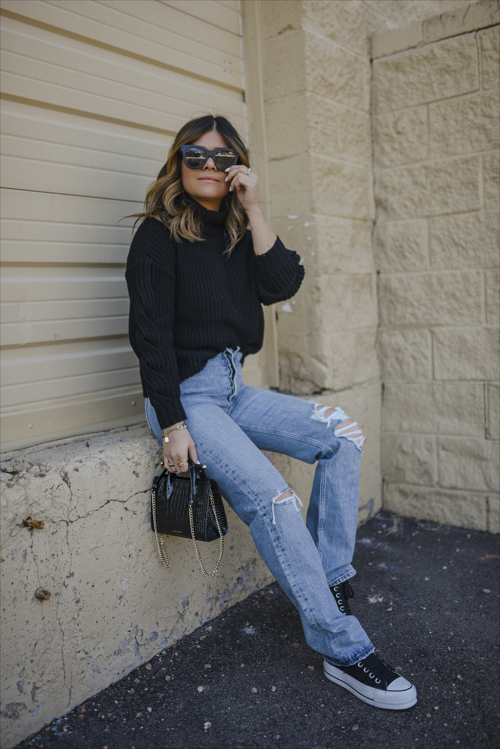Carolina Hellal of Chic Talk wearing a cutout knit sweater and agolde jeans via Bloomingdales. Black Converse and strathberry bag