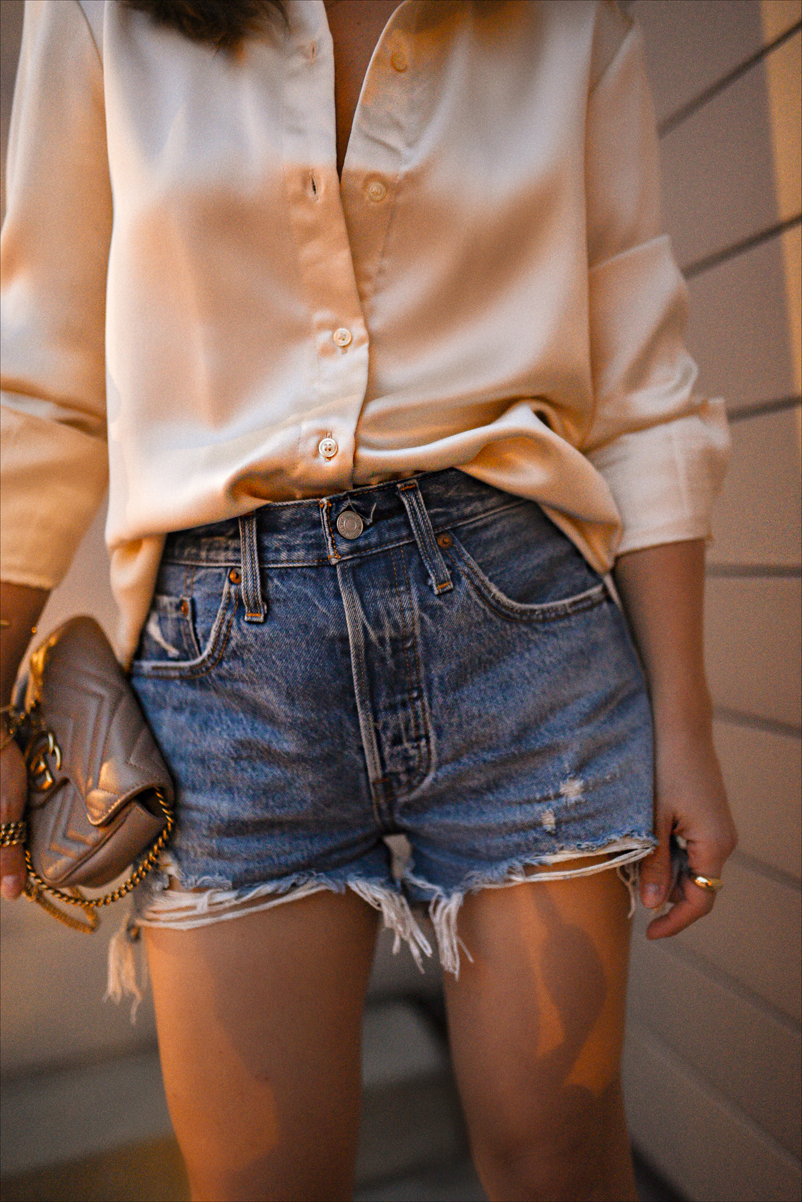 Carolina Hellal of Chic Talk wearing Levi's 501 Denim shorts, a silk button-down shirt, gold strappy heeled sandals, and A gucci Marmont super mini shoulder bag. 