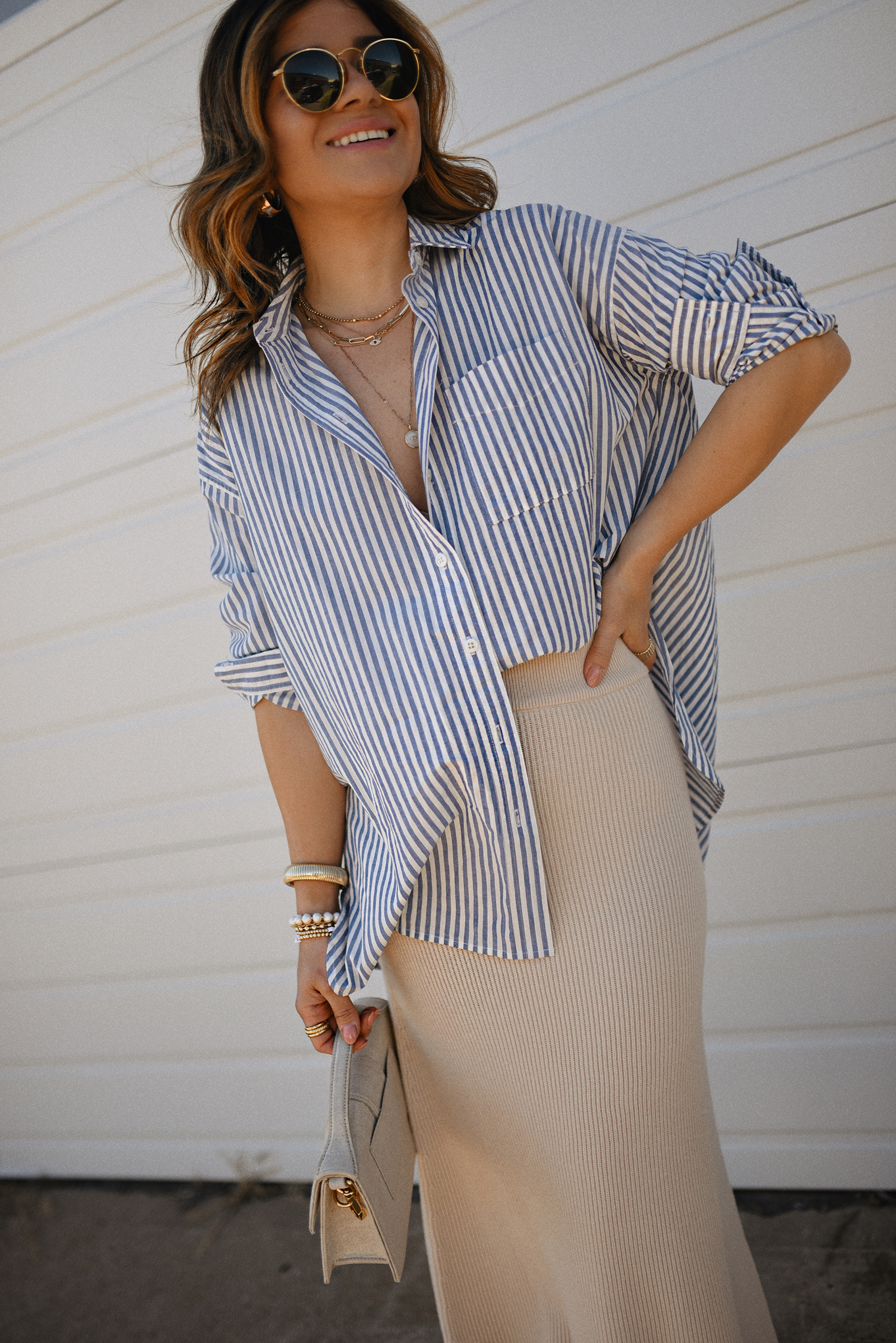 Carolina Hellal of Chic Talk wearing a Madewell striped oversize shirt, a Sezane beige skirt, black sandals and Le grand Bambino bag from Jacquemus