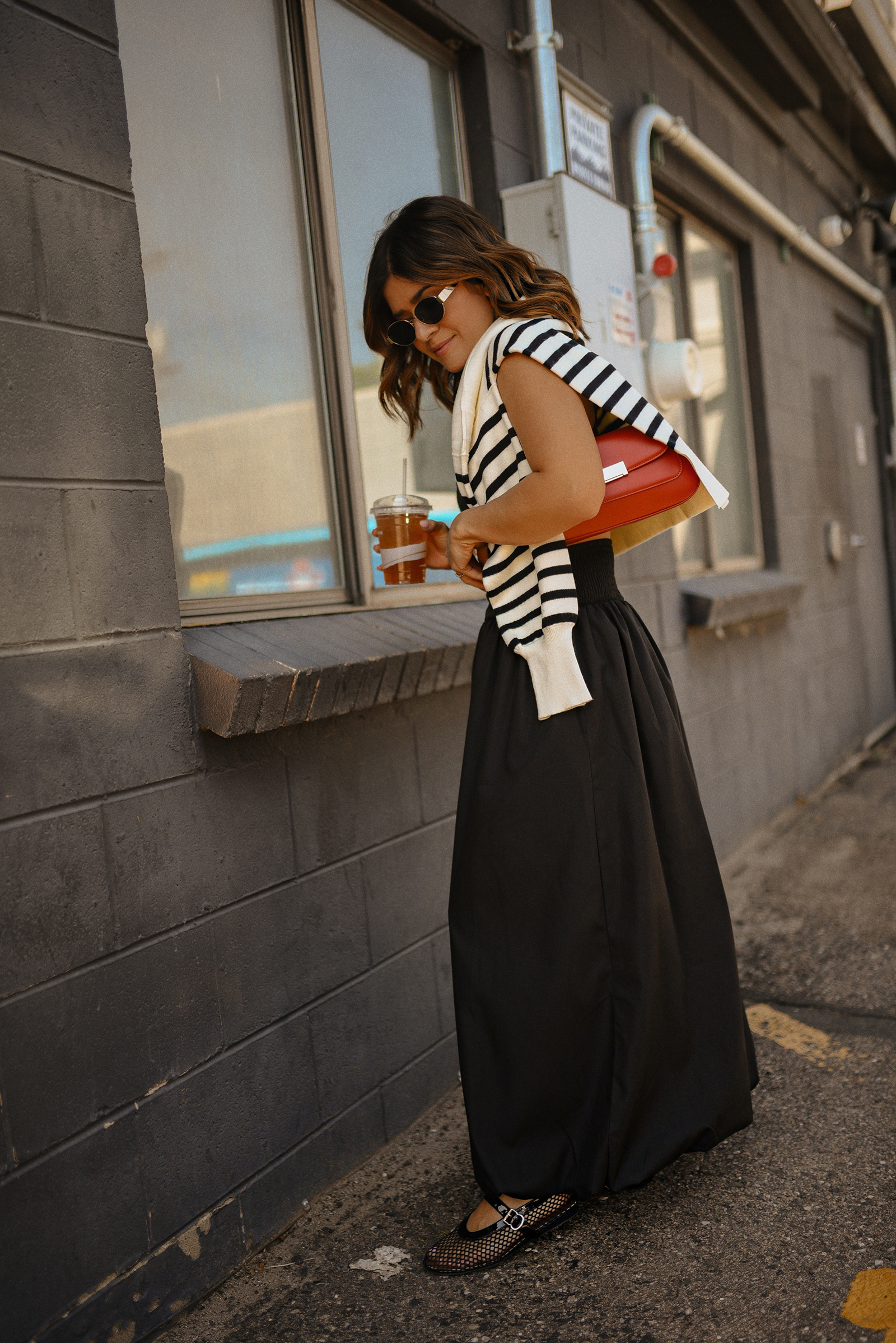 Carolina Hellal of Chic Talk wearing a bubble hem maxi skirt, a stripped sweater, a mesh Mary Jane flats and sunglasses via Amazon, a black crop top from Target and red handbag via Anthropologie