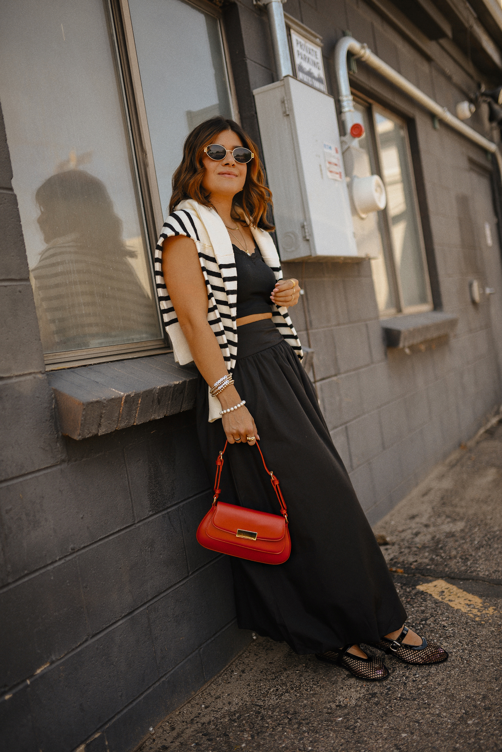 Carolina Hellal of Chic Talk wearing a bubble hem maxi skirt, a stripped sweater, a mesh Mary Jane flats and sunglasses via Amazon, a black crop top from Target and red handbag via Anthropologie