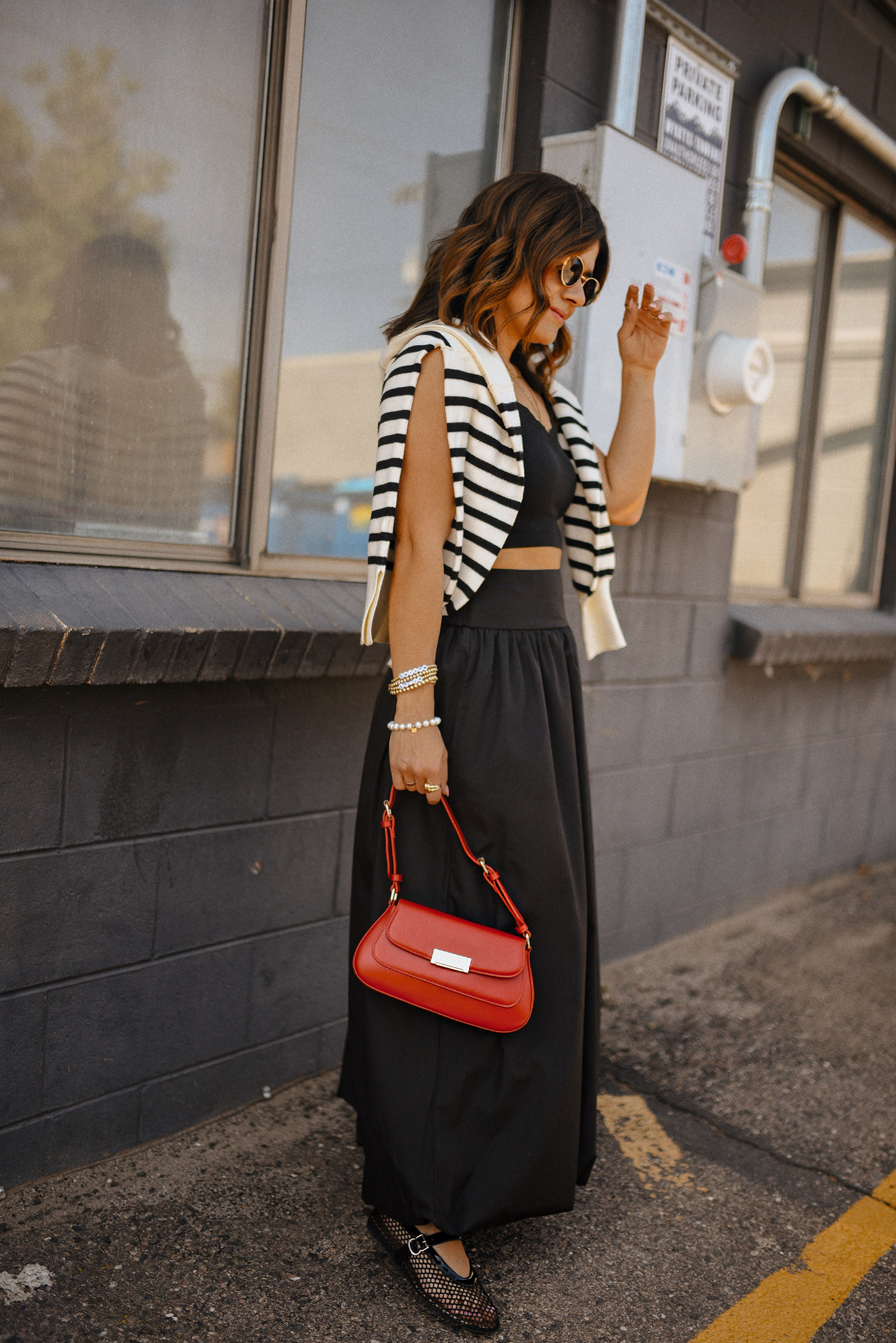 Carolina Hellal of Chic Talk wearing a bubble hem maxi skirt, a stripped sweater, a mesh Mary Jane flats and sunglasses via Amazon, a black crop top from Target and red handbag via Anthropologie