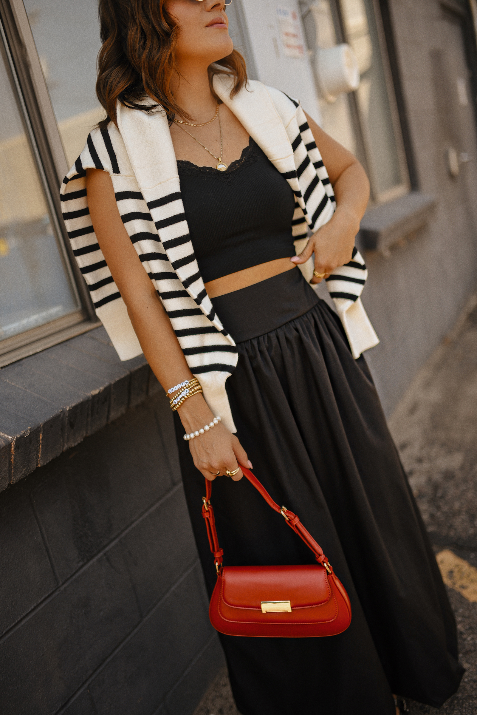 Carolina Hellal of Chic Talk wearing a bubble hem maxi skirt, a stripped sweater, a mesh Mary Jane flats and sunglasses via Amazon, a black crop top from Target and red handbag via Anthropologie