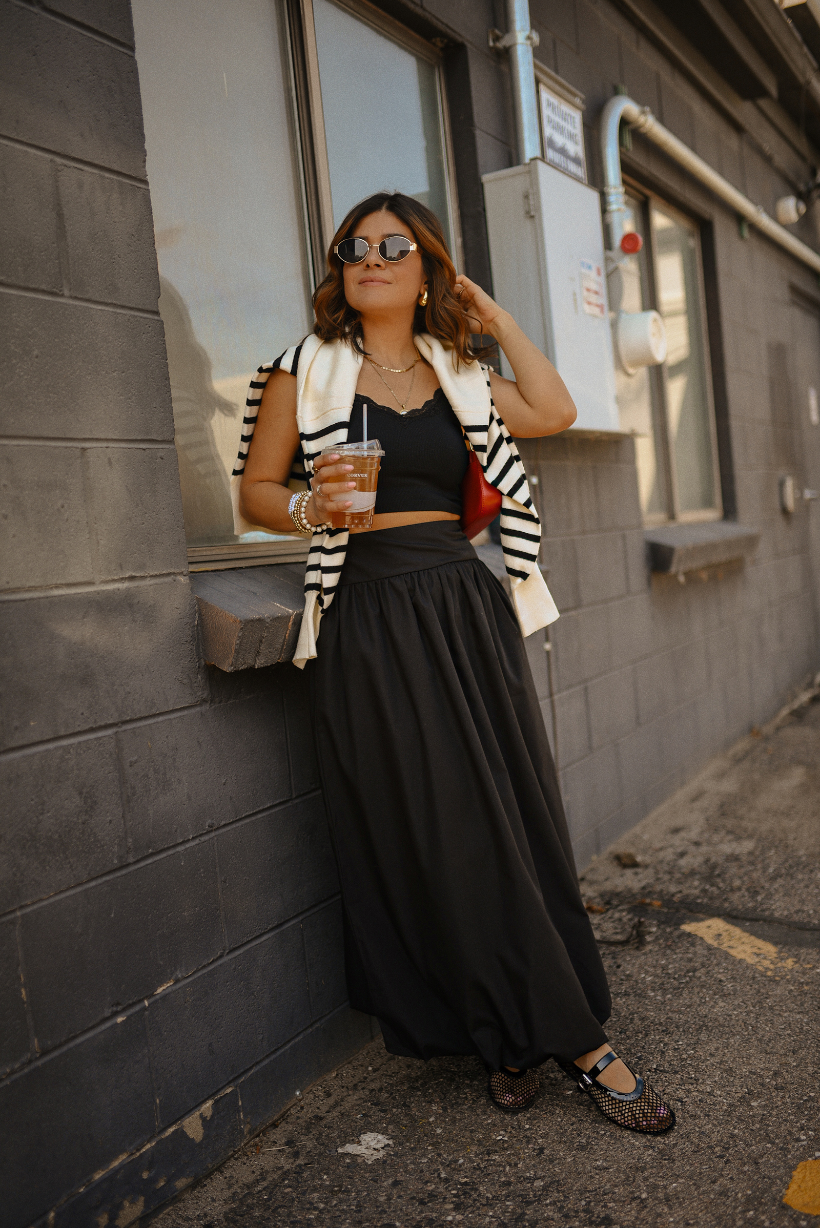 Carolina Hellal of Chic Talk wearing a bubble hem maxi skirt, a stripped sweater, a mesh Mary Jane flats and sunglasses via Amazon, a black crop top from Target and red handbag via Anthropologie